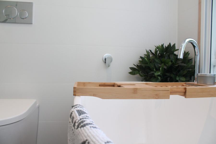 Timber bath caddy over white bathtub with plant beside a bathroom window