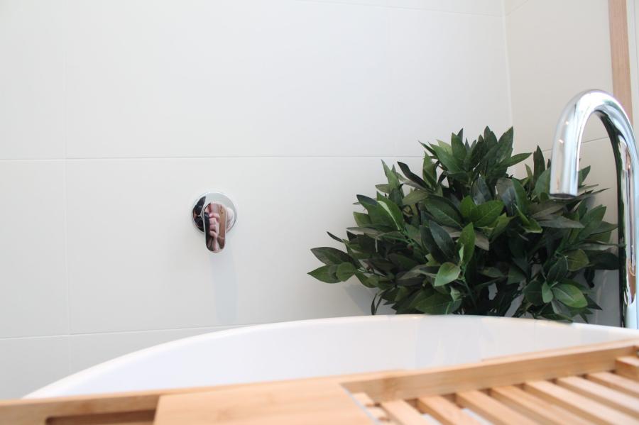 White bathtub with chrome tap and timber bath caddy beside greenery
