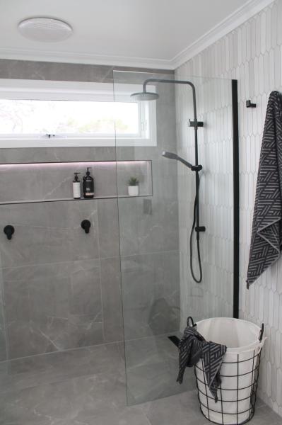 Modern walk-in shower with grey tiles, frameless glass screen and black tapware