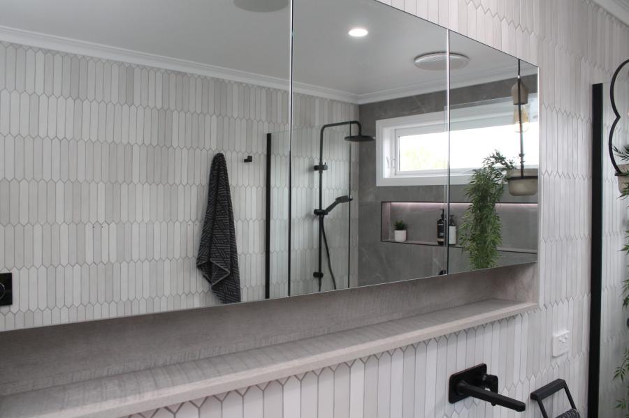Modern bathroom mirror reflecting walk-in shower with vertical white tiles and black tapware