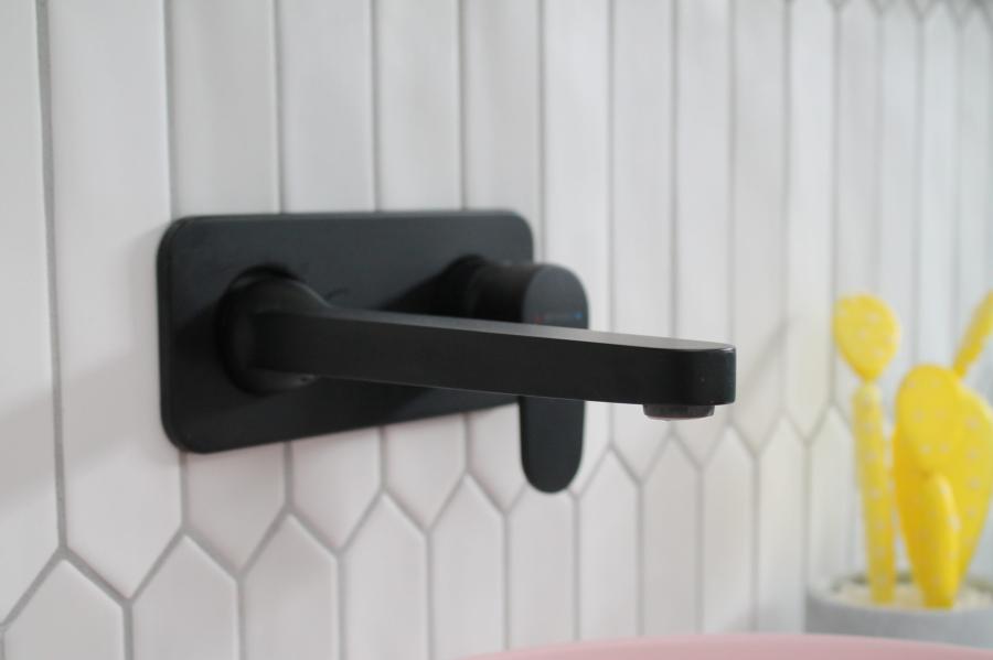 Matte black wall-mounted bathroom tap on white patterned tiles