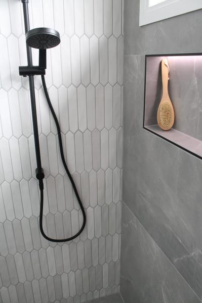 Black shower head in white tiled shower with recessed niche and grey wall tiles