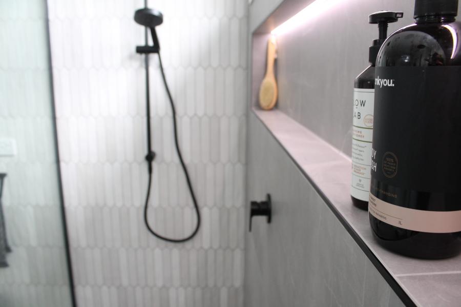 Walk-in shower with black tapware and recessed niche in a modern tiled bathroom