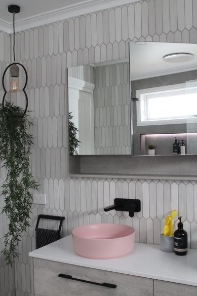 Modern bathroom vanity with pink basin, black tapware and textured white wall tiles