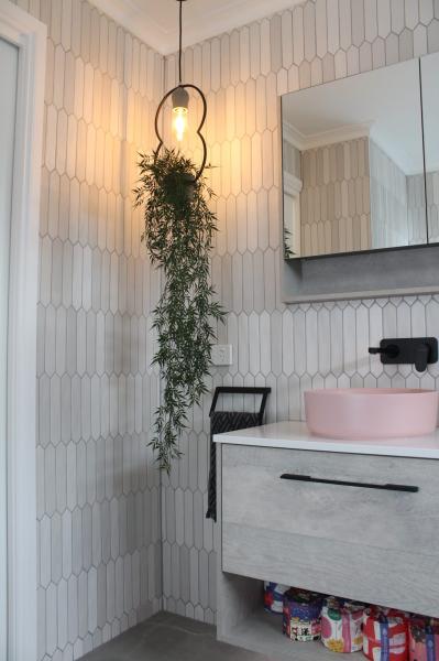 Modern bathroom vanity with pink basin, vertical white tiles, wall mirror and pendant light