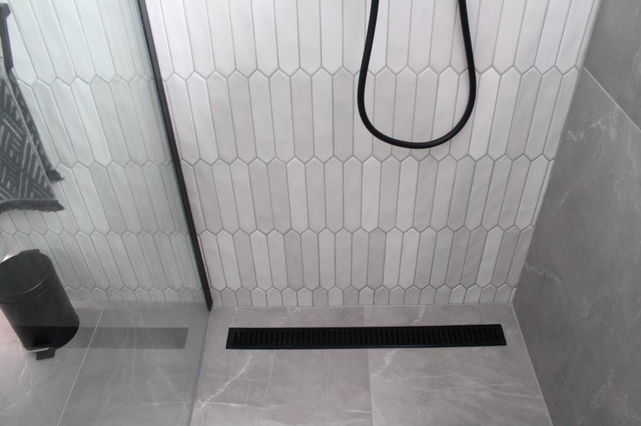 Walk-in shower with white feature tiles, grey floor tiles and black linear drain