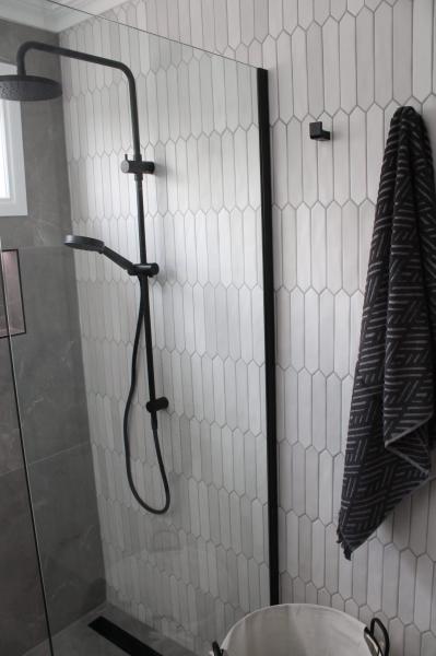 Walk-in shower with white vertical tiles, black tapware and frameless glass screen