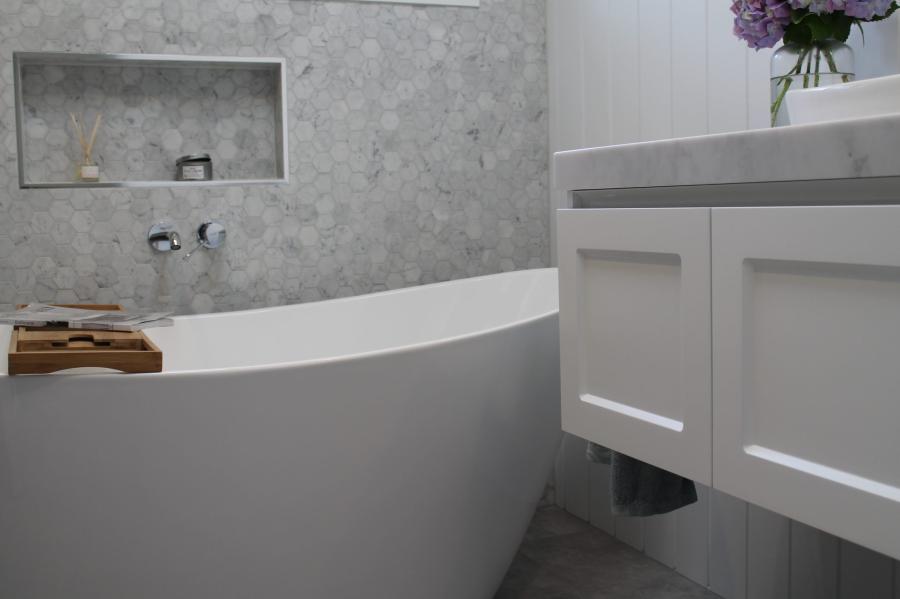 Freestanding bath beside white vanity in a modern grey tiled bathroom