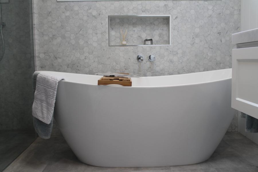 Freestanding white bath in a modern grey tiled bathroom with recessed wall niche