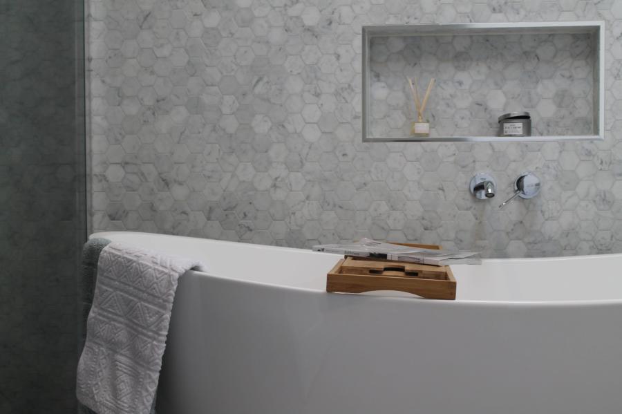 Freestanding white bath against grey tiled wall with recessed niche and chrome tapware