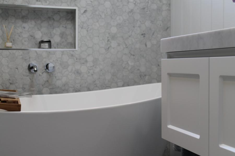 Freestanding white bath beside a white vanity in a grey tiled modern bathroom