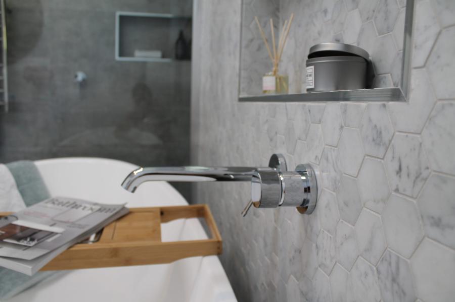 Chrome wall-mounted bath spout beside freestanding bath and tiled niche