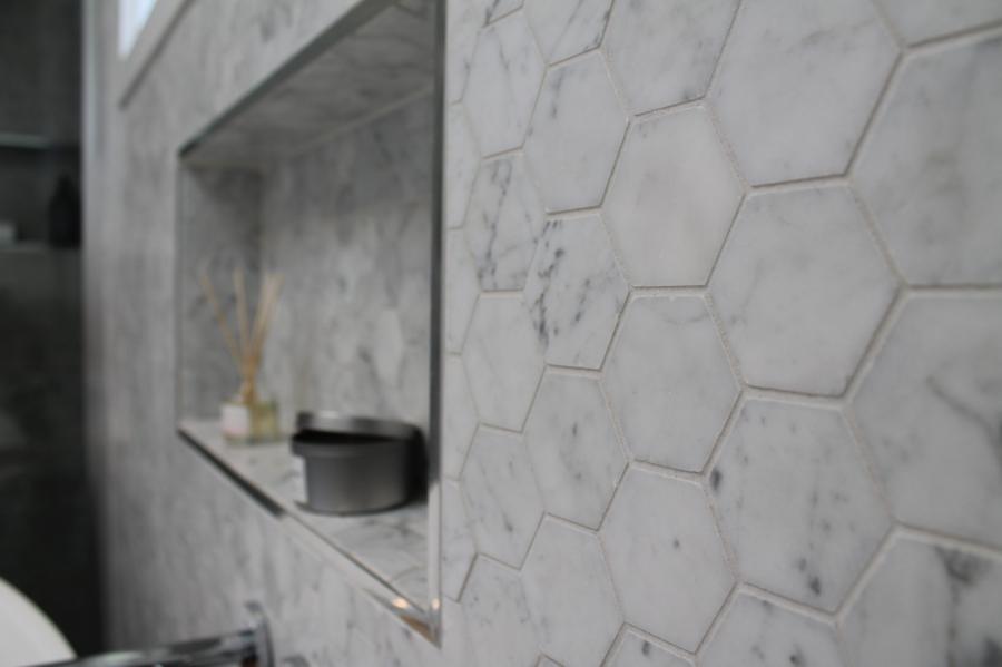 Close-up of a tiled shower niche with white hexagon marble-look wall tiles