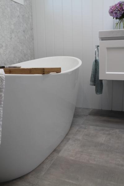 Freestanding white bath in a modern bathroom with grey floor tiles and timber bath caddy