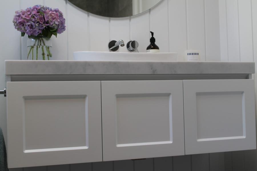 White shaker-style bathroom vanity with basin, round mirror and purple flowers