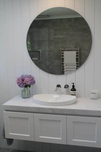 White bathroom vanity with round mirror, vessel basin and grey tiled wall