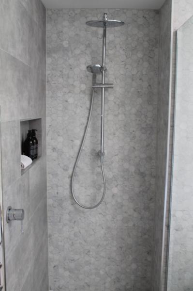 Walk-in shower with grey wall tiles, niche shelf and chrome handheld shower