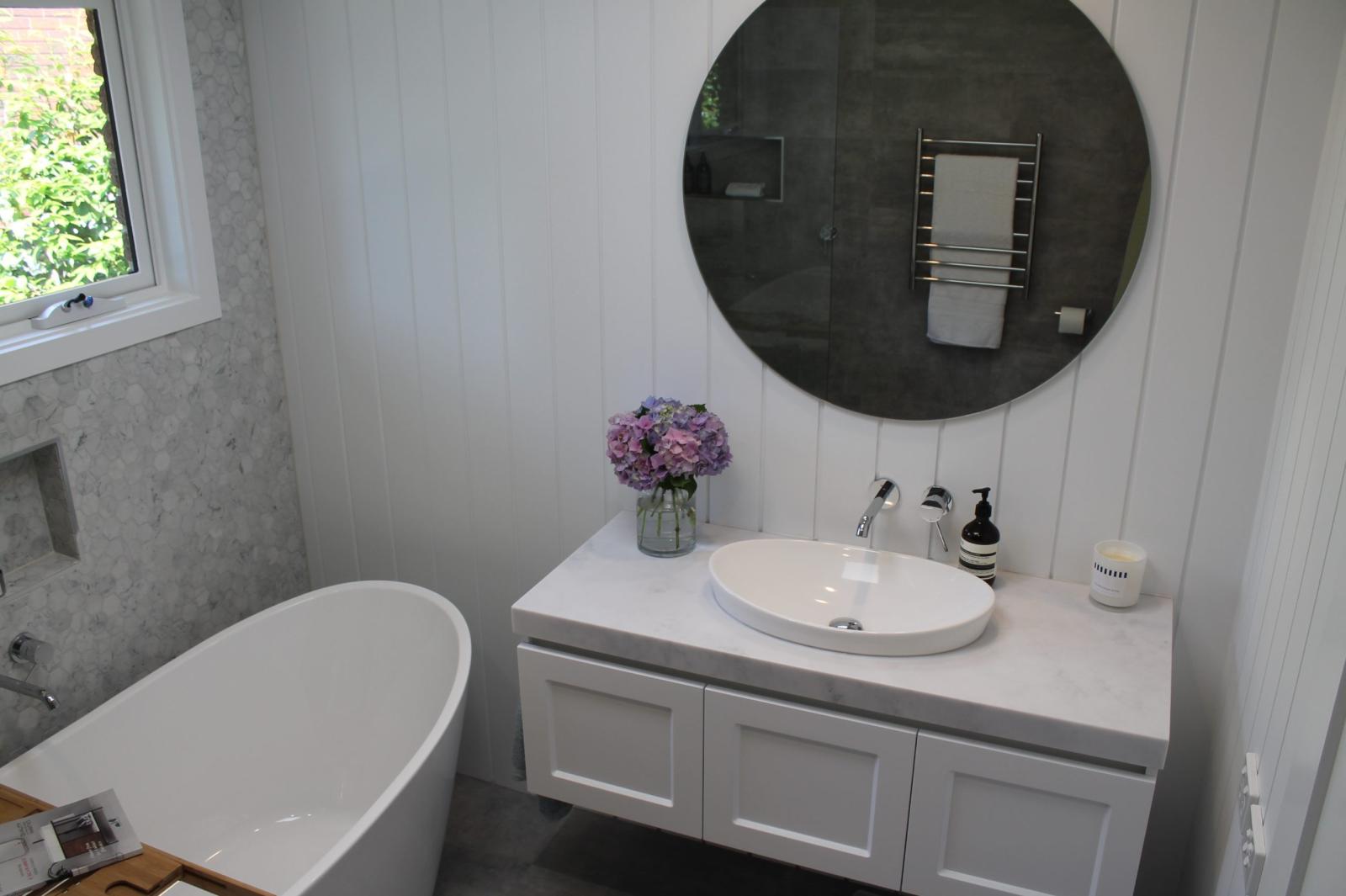 Modern bathroom with white vanity, round mirror, freestanding bath