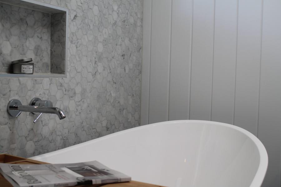 Freestanding white bath beside grey tiled wall niche in a modern bathroom