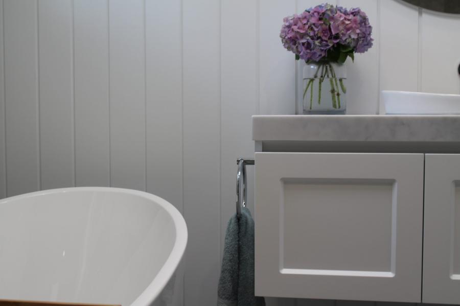 White bathroom vanity beside a freestanding bath with flowers on the benchtop