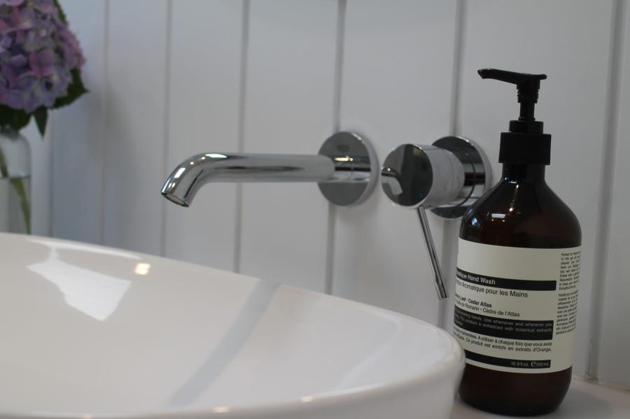 Chrome wall-mounted bathroom tap beside basin and soap dispenser