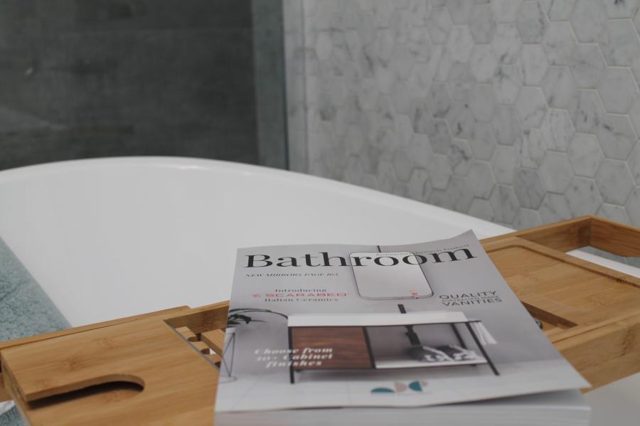 Bathroom design magazine on a timber bath caddy beside a white bathtub