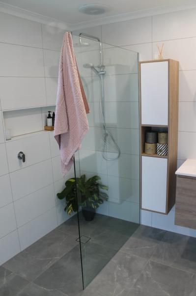 Modern walk-in shower with frameless glass screen, white wall tiles and built-in storage
