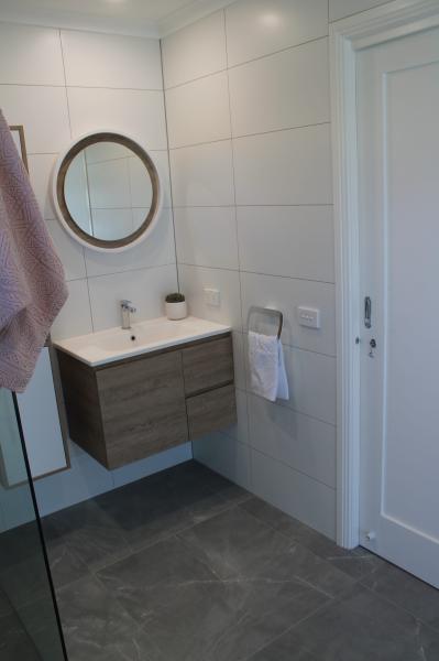 Modern bathroom with floating timber vanity, round mirror, white wall tiles and grey floor tiles