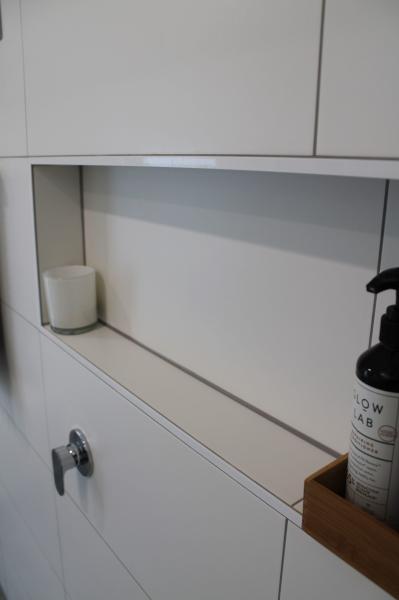 White built-in bathroom storage niche with cabinetry and timber tray