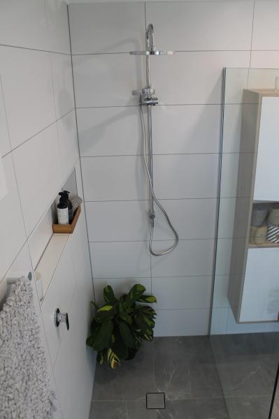 Modern walk-in shower with white wall tiles, chrome handheld shower, and grey floor tiles
