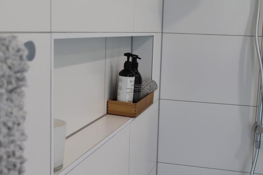 Recessed shower niche with toiletry shelf in a white tiled bathroom