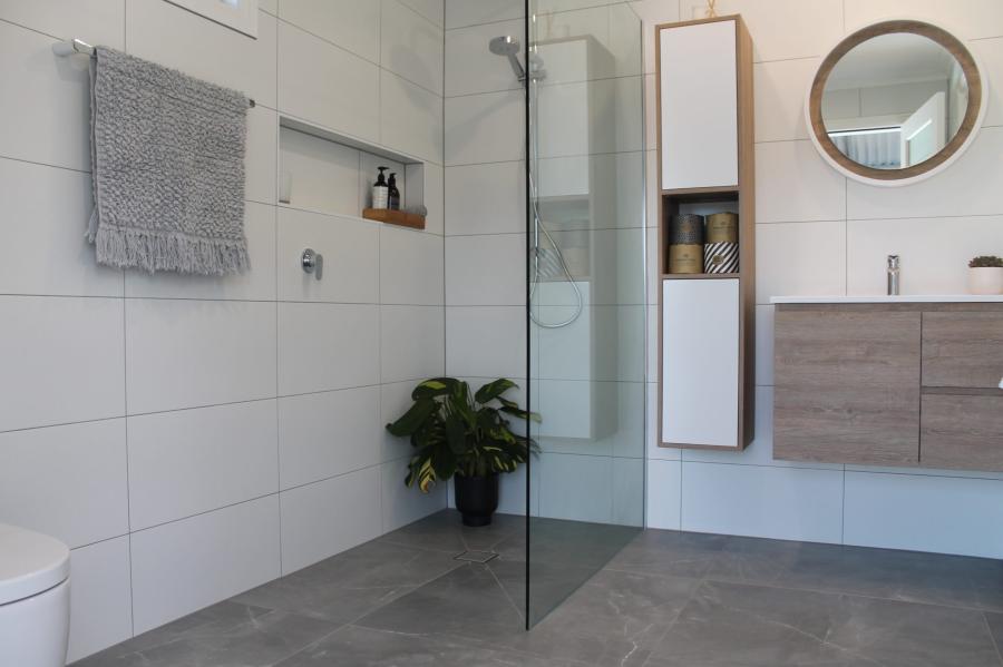 Modern white tiled bathroom with walk-in glass shower, timber vanity and round mirror