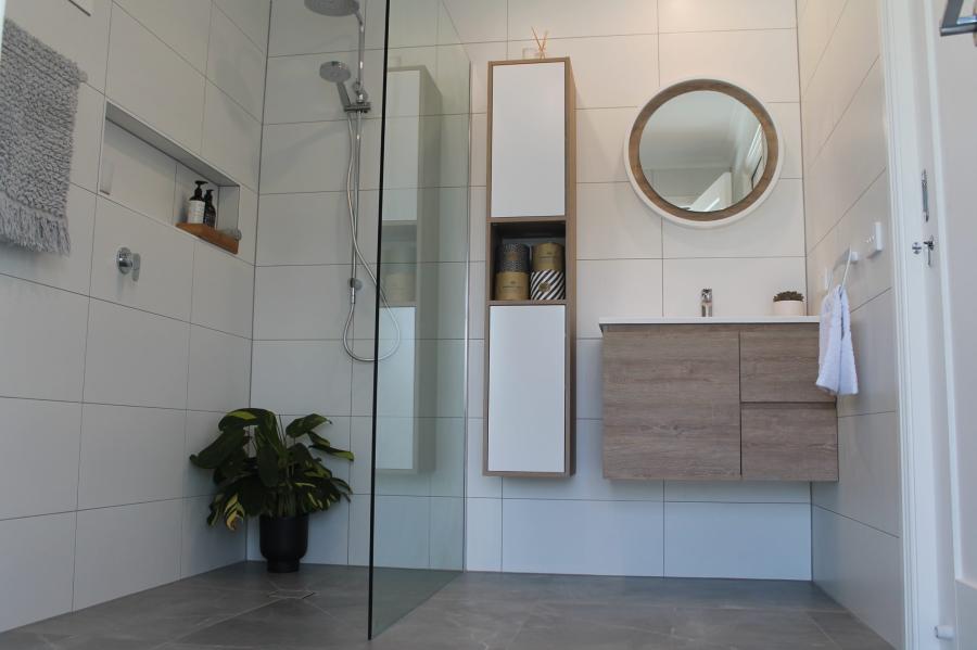Modern white tiled bathroom with walk-in shower, floating vanity and round mirror
