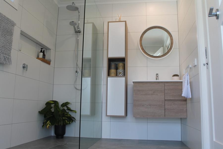 Modern white bathroom with floating timber vanity, round mirror and walk-in glass shower
