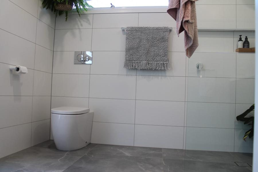 Modern white tiled bathroom with wall-faced toilet, towel rail and shelf