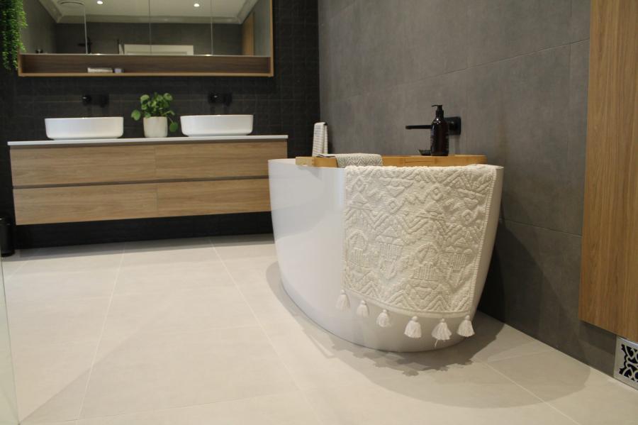 Freestanding textured white bath beside timber vanity in a modern grey bathroom