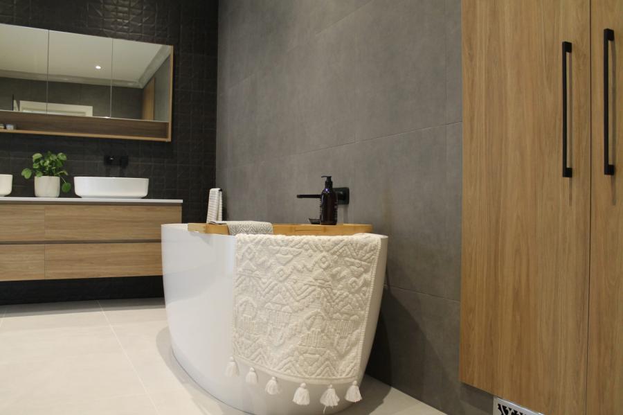 Freestanding bath with textured white finish in a modern bathroom with timber vanity and black tapware
