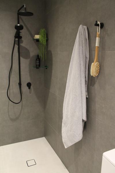 Modern walk-in shower with grey wall tiles, black shower set and white towel