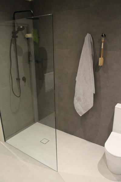 Modern walk-in shower with frameless glass screen, grey wall tiles and white towel