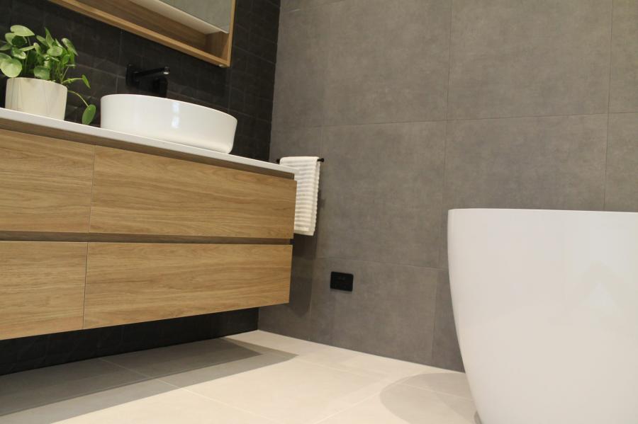 Floating timber vanity beside freestanding bath in a modern grey bathroom