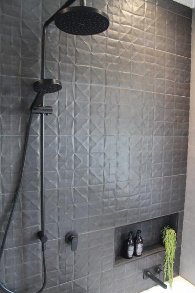 Modern walk-in shower with dark textured wall tiles, black rain shower and recessed niche