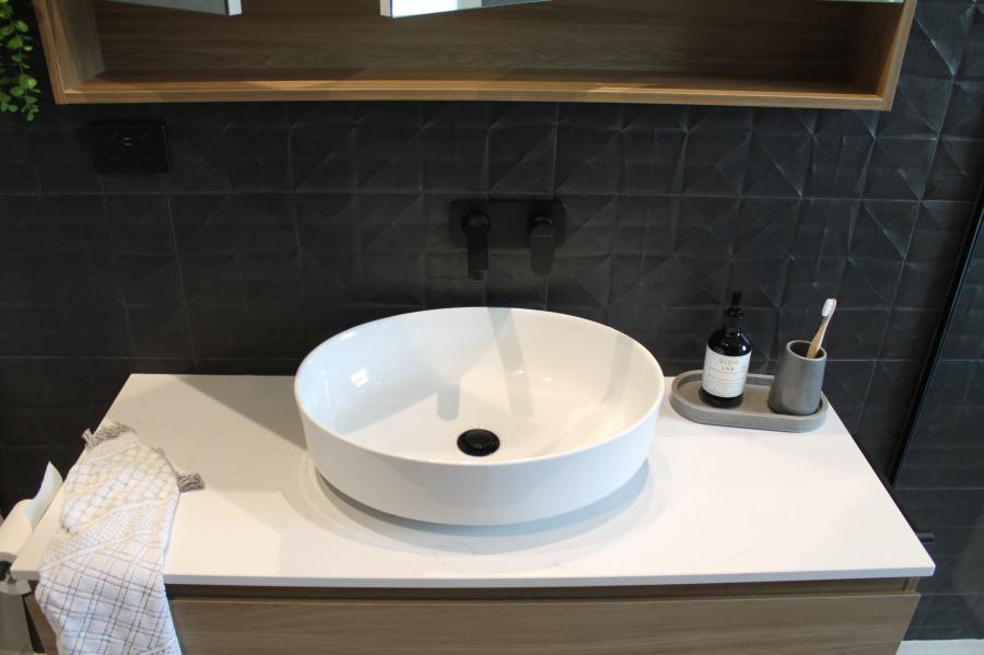 Round white vessel basin on a modern vanity with dark wall tiles and black tapware