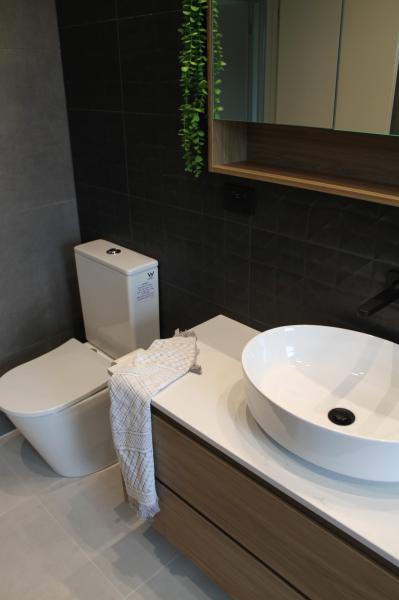 Modern bathroom vanity with vessel basin beside wall-faced toilet and dark tiled feature wall