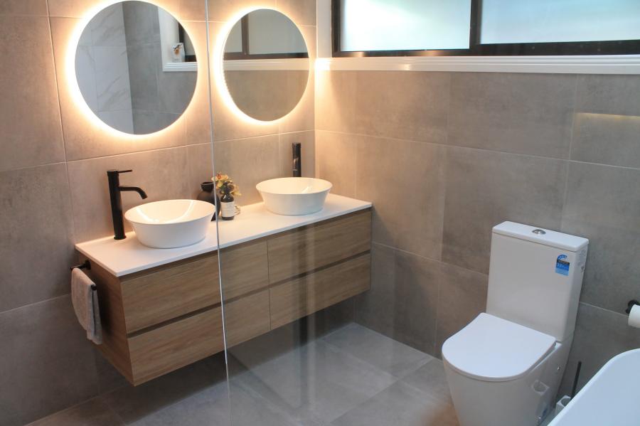 Modern bathroom with double vanity, round mirrors, matte black tapware and wall-faced toilet