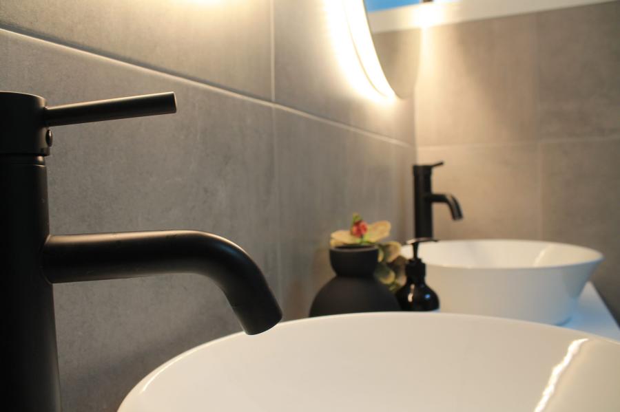 Matte black bathroom tap beside a white basin in a modern tiled bathroom