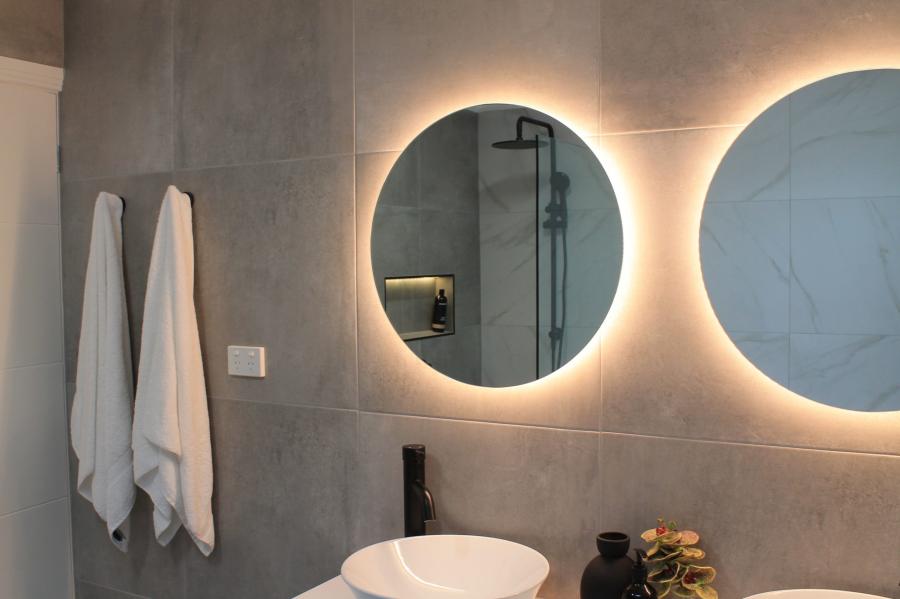 Modern bathroom vanity with two backlit round mirrors, wall tiles and white towels