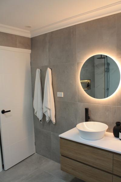 Modern bathroom vanity with round illuminated mirror and grey wall tiles