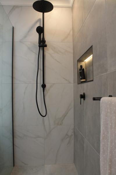 Walk-in shower with matte black tapware, niche lighting and marble-look wall tiles