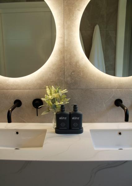 Double vanity bathroom with two basins, round backlit mirrors and black tapware