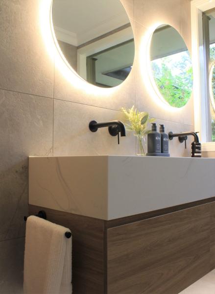 Modern bathroom vanity with round illuminated mirror, black tapware and beige wall tiles
